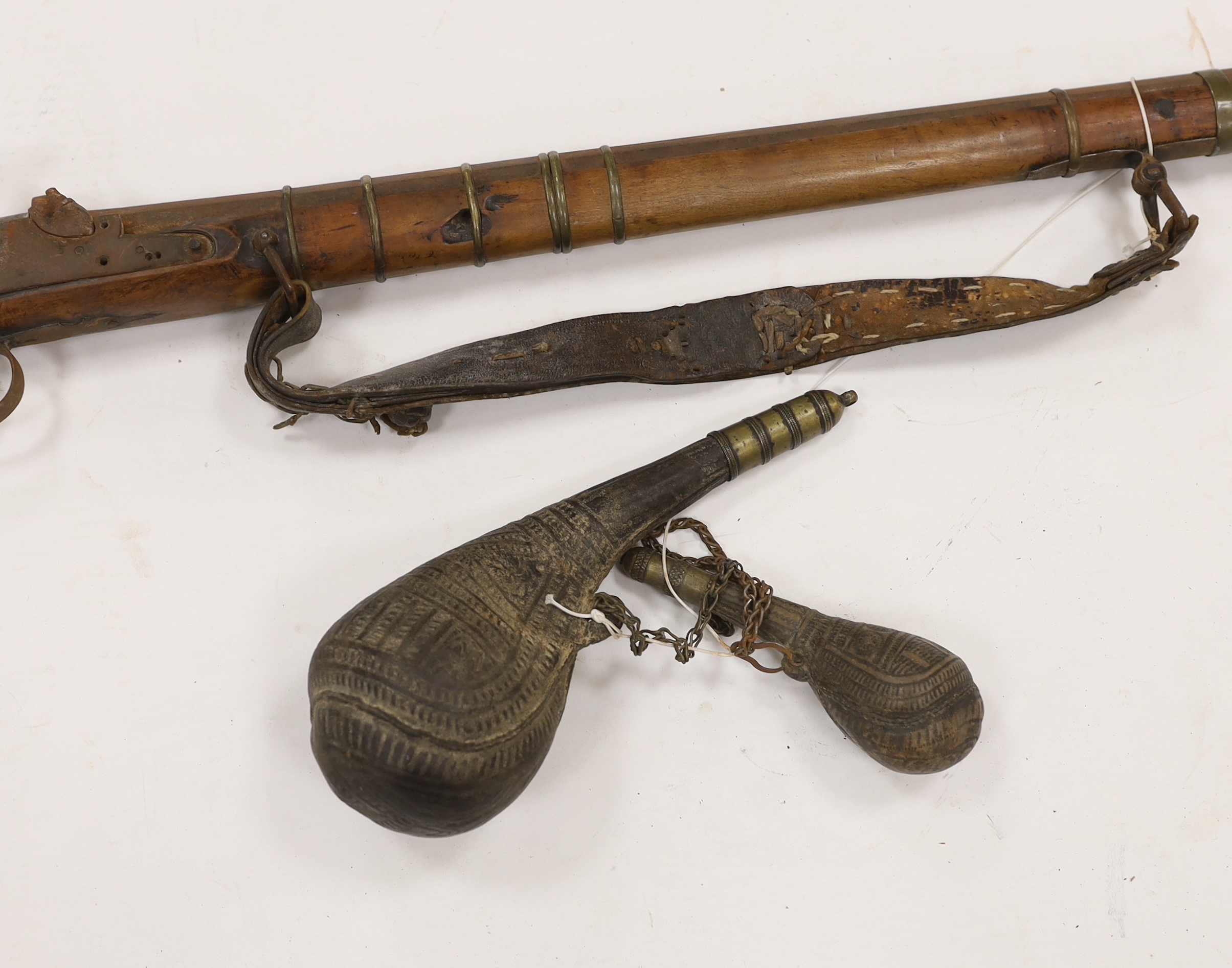 An Afghan percussion rifle with octagonal barrel and brass mounts, barrel 105.5cm, together with two leather powder flasks